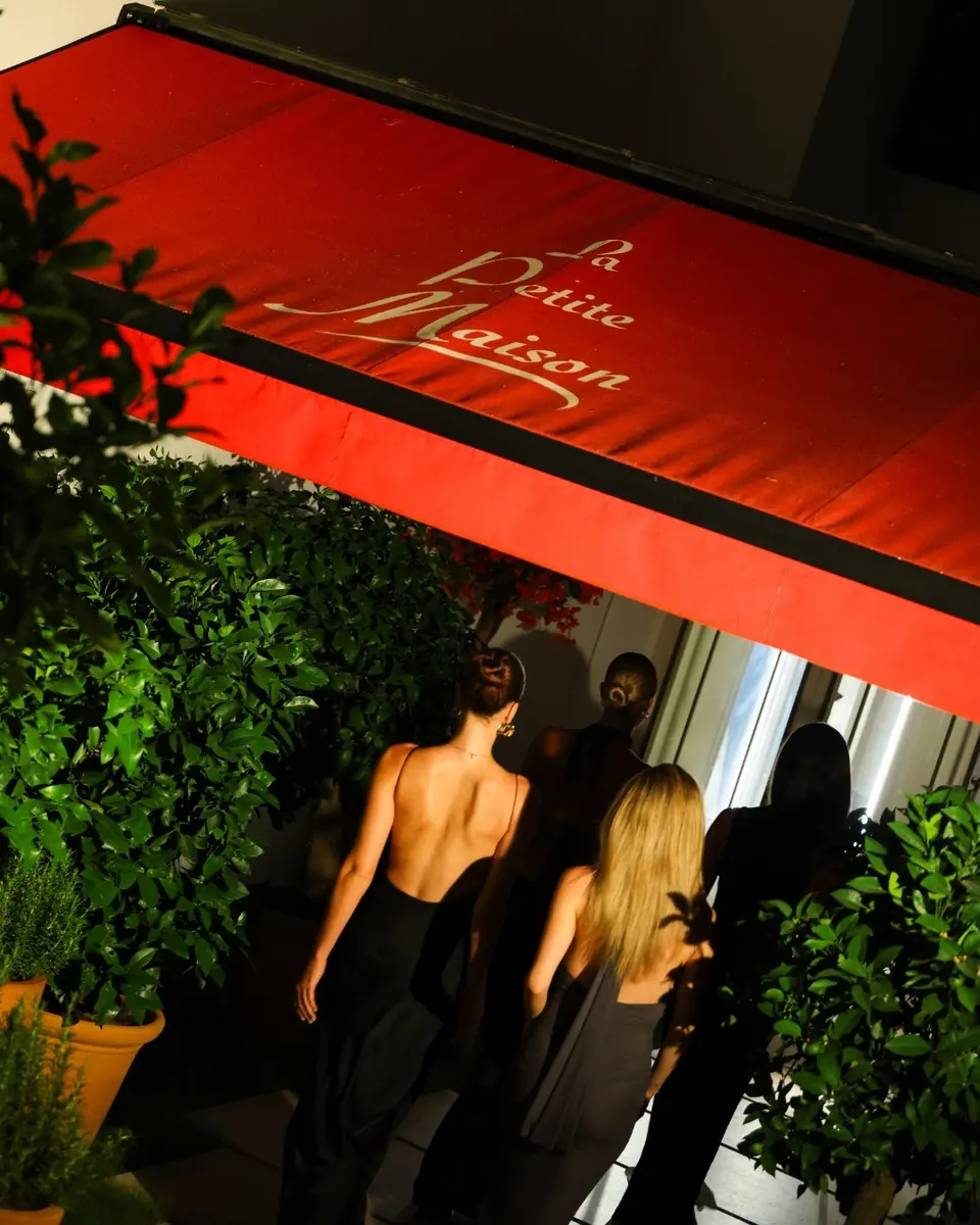 Guests arriving at night under the red La Petite Maison awning