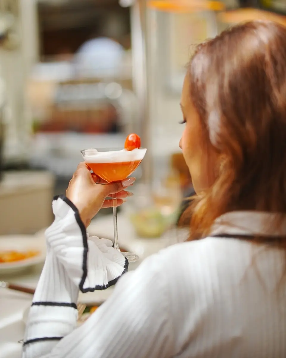 A guest raising a coupe cocktail garnished with a cherry