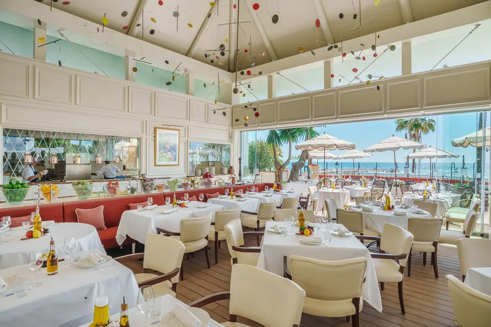 The dining room at lunchtime: white tablecloths, red banquettes, art on the walls and the sea through open glass doors