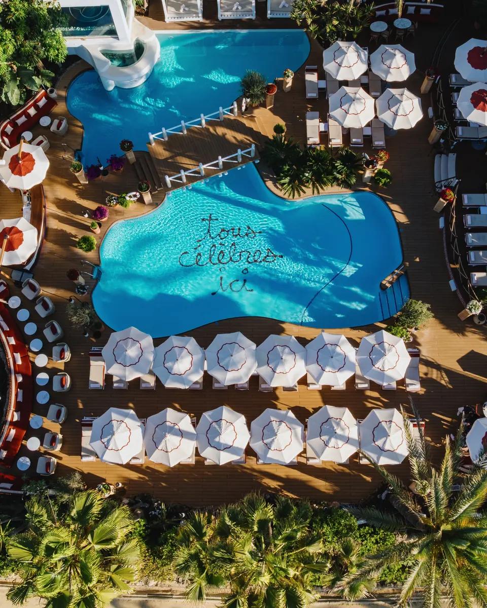 Aerial view of the pool with ‘tous célèbres ici’ written on its floor, ringed by white parasols