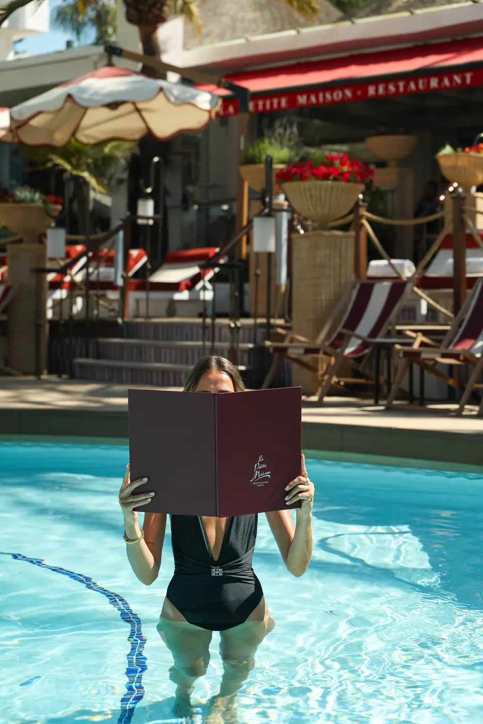 A guest in the pool reading the LPM menu, the restaurant terrace behind