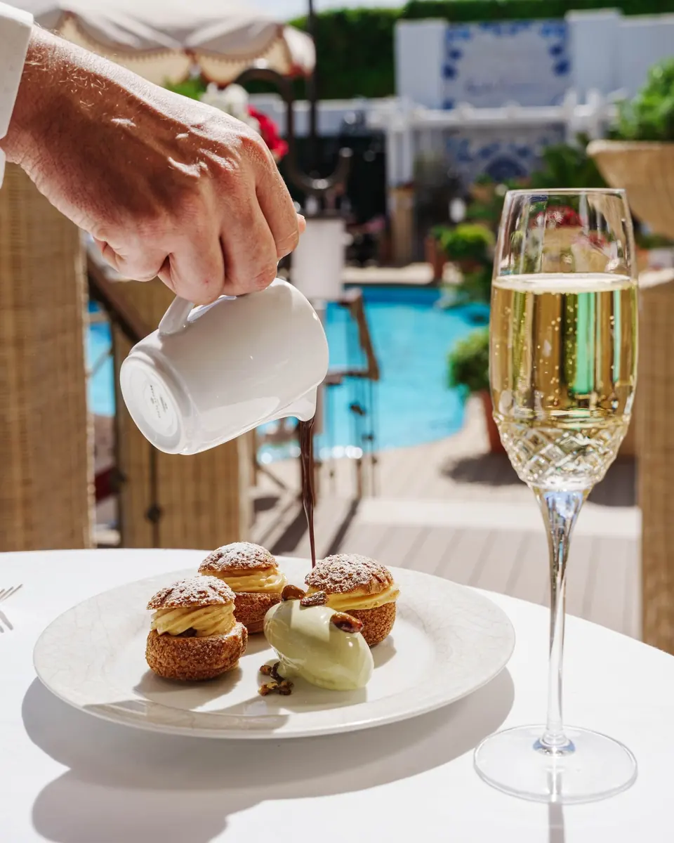 Profiteroles with pistachio ice cream beside a glass of champagne, the pool behind