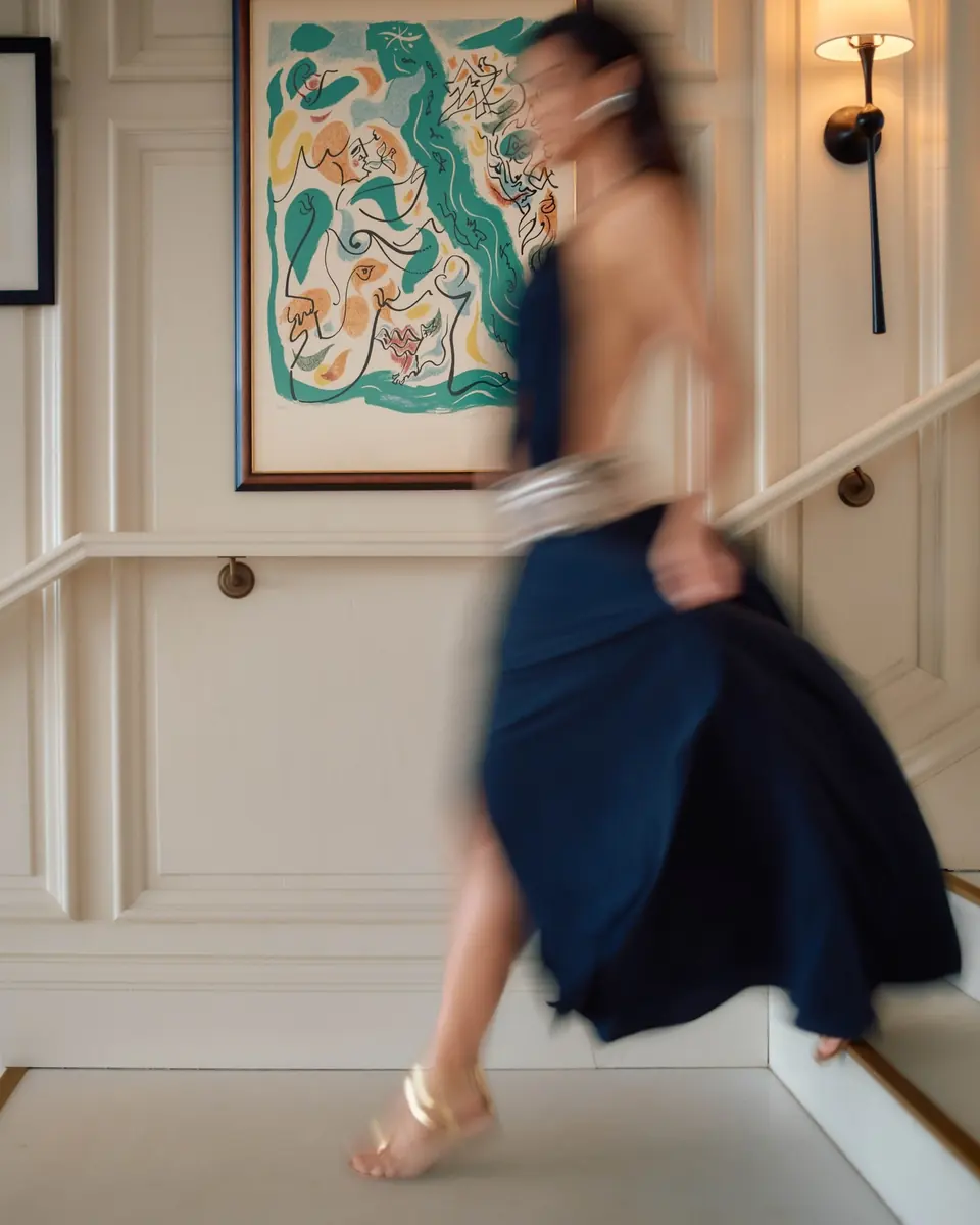 A woman in a navy dress hurrying up the stairs past a colourful painting