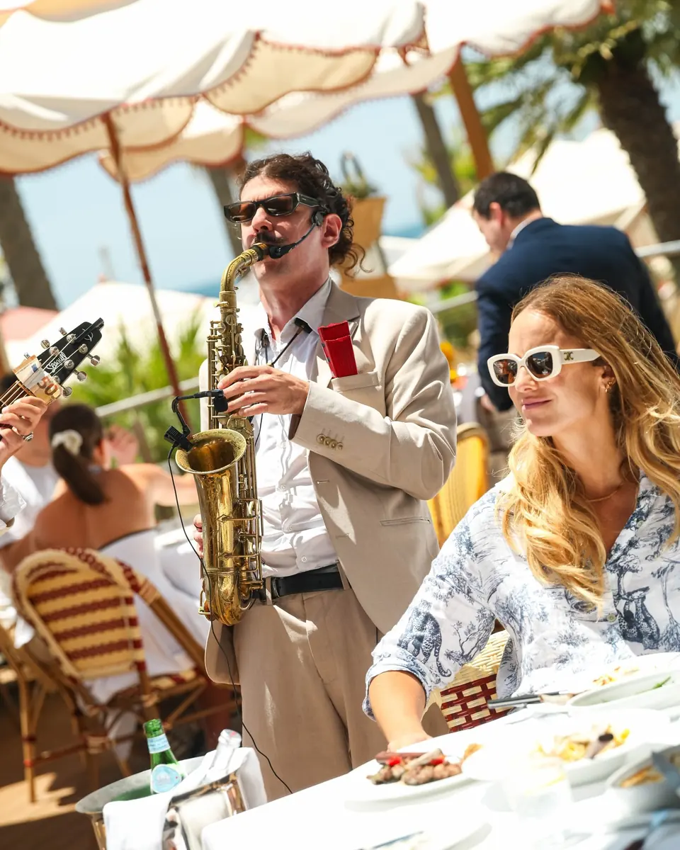 A saxophonist playing beside a guest in sunglasses on the terrace