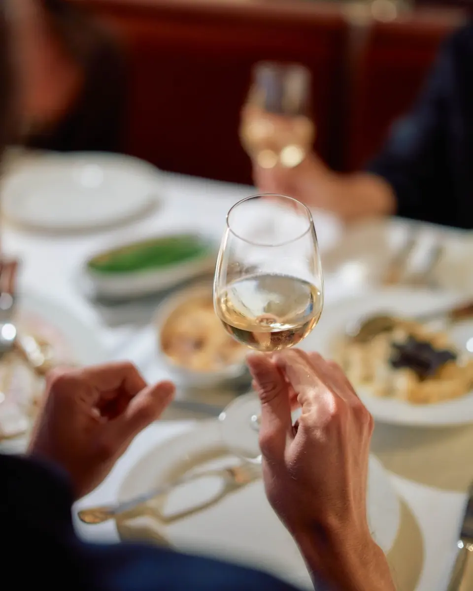 A glass of white wine raised over a lunch table